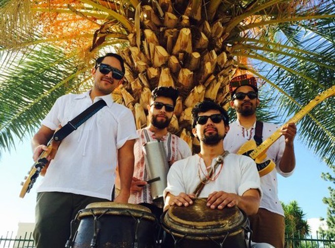 the band QUITAPENAS posing with their instruments under a palm tree
